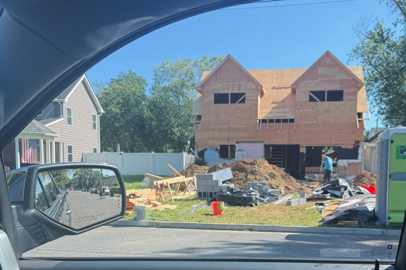 Brick residential home under construction with wood framing, peaked roofs, and foundation work visible
