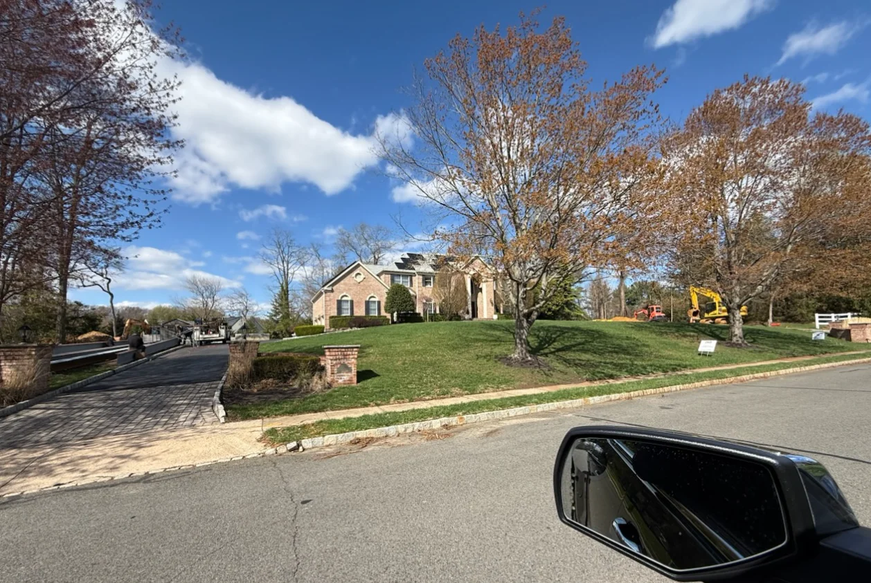 Newly paved asphalt driveway with brick edging and fresh sod lawn in front of brick home