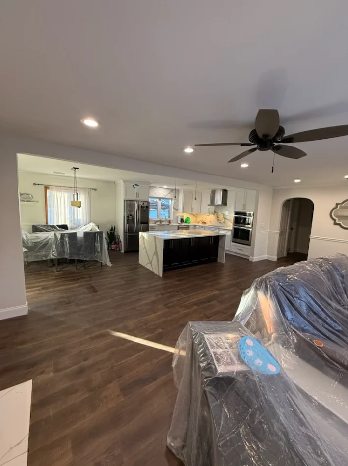 Open concept kitchen with white cabinets, black island, stainless appliances, and dark wood flooring during construction