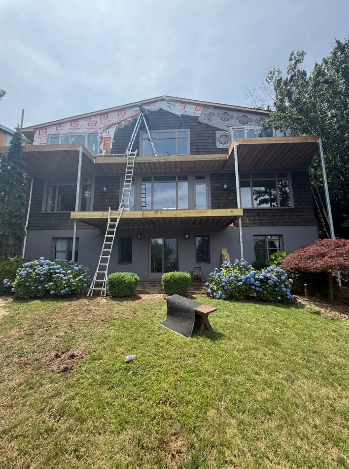 Multi-story home with dark siding, new windows, and yellow deck framing under construction