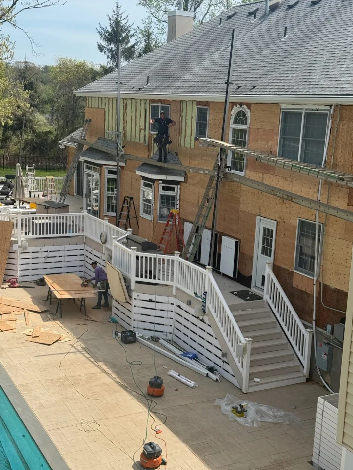 Multi-level white vinyl deck with composite decking and stairs under construction on brick home