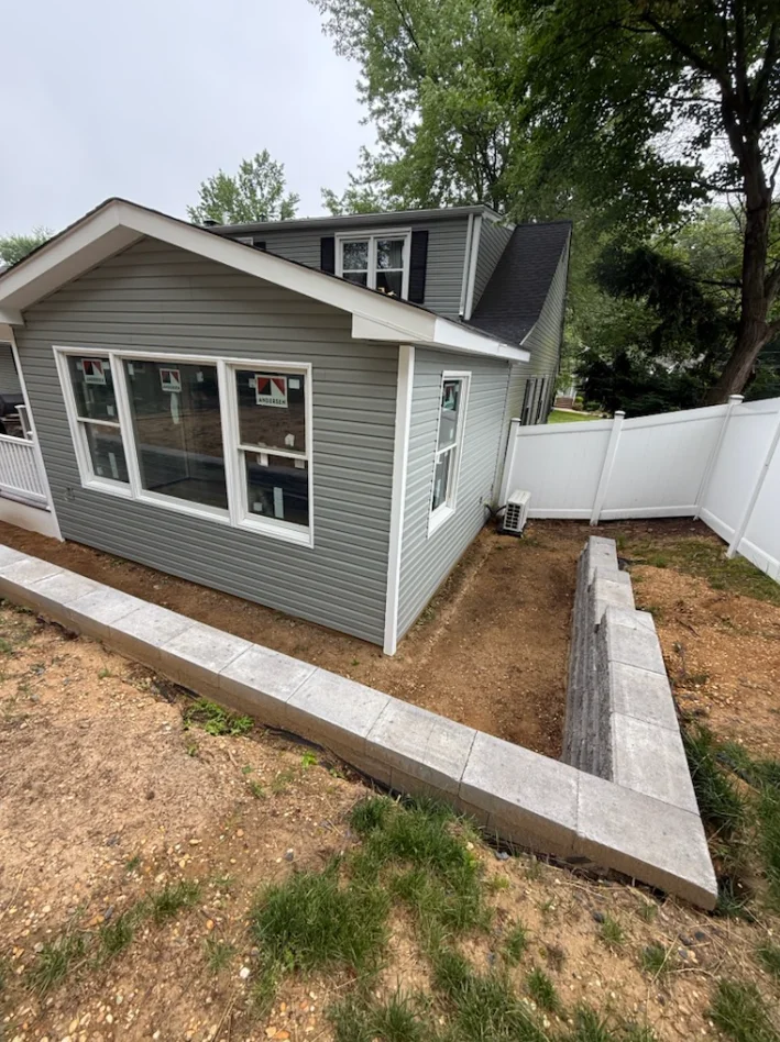 Gray vinyl siding addition with large windows, concrete foundation, and white vinyl fence