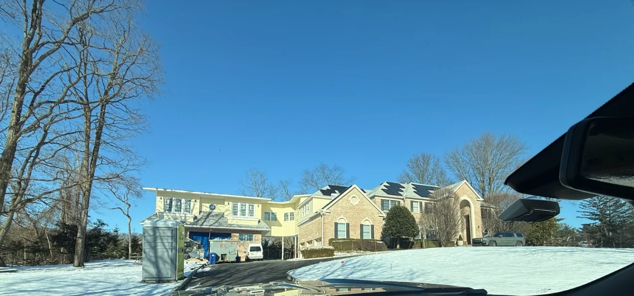 Newly installed gutters running along the roofline of a large single-family Colonial home in Holmdel, NJ. Downspouts extend to ground level with water directed away from the home's foundation and landscaping.