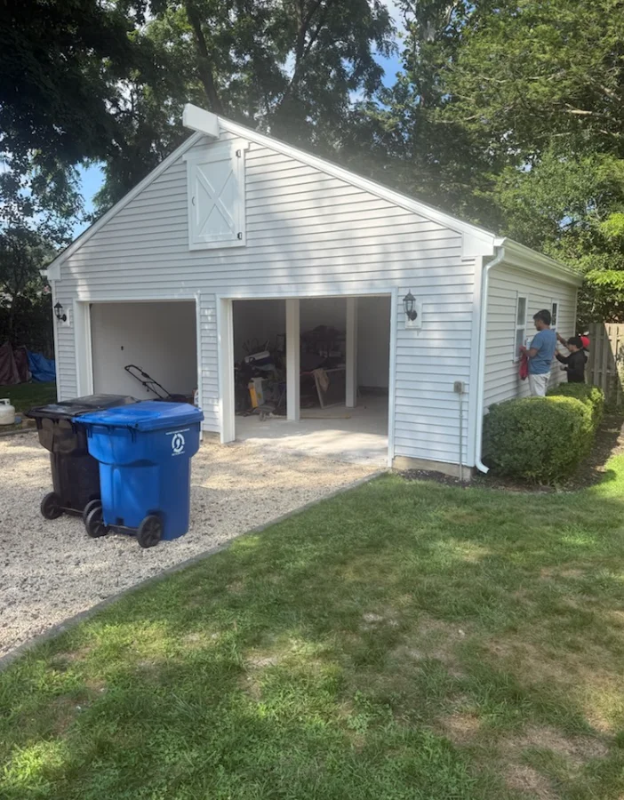 A repaired gutter section on a large single-family home in Holmdel, NJ, with a cleared downspout and resealed joints visible along the roofline. Mature trees in the background reflect the typical tree-canopy conditions that affect gutter performance in the area.